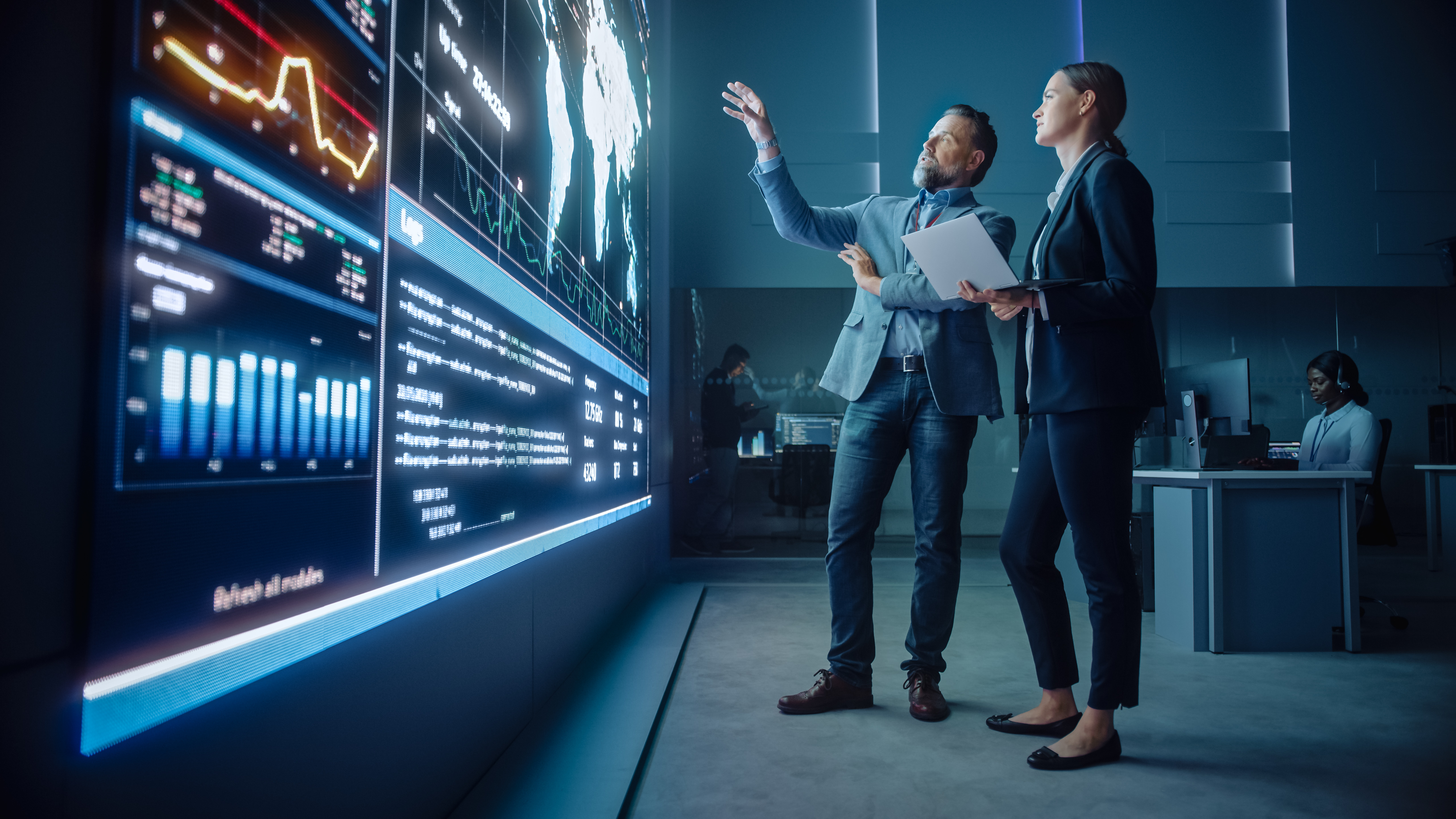 Two people look at shipping routes on a futuristic video wall